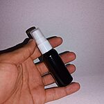 A hand holding a small dark bottle with a white pump against a pale background