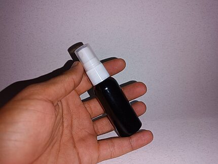 A hand holding a small dark bottle with a white pump against a pale background