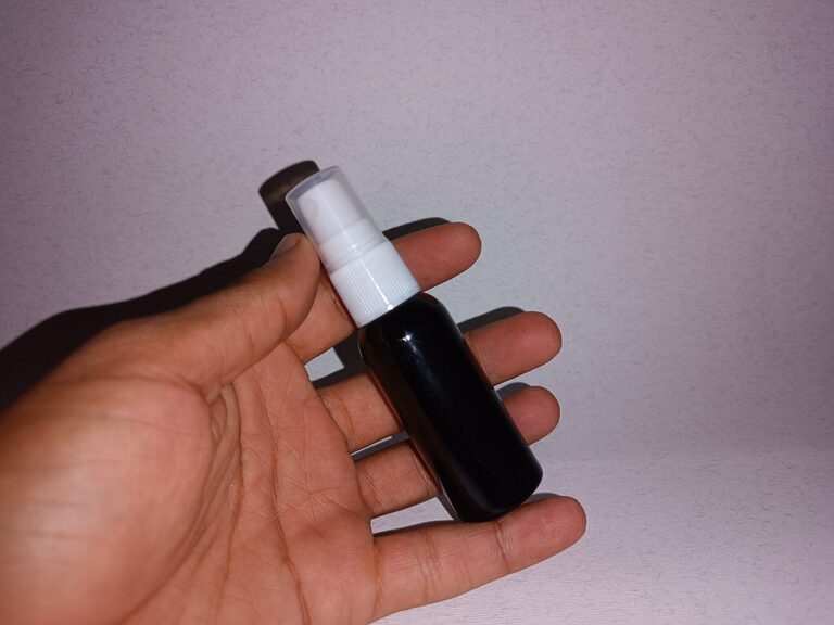 A hand holding a small dark bottle with a white pump against a pale background