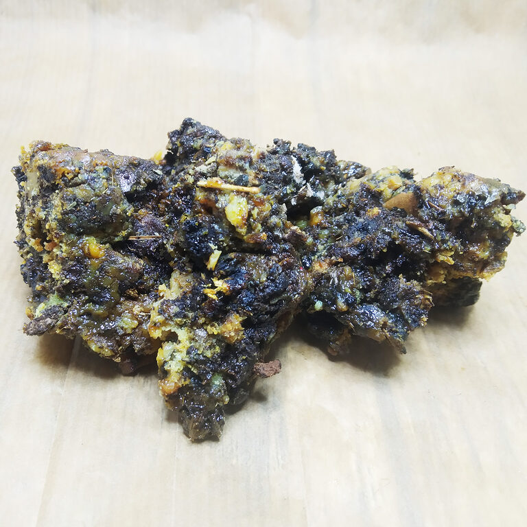 Close-up of dark glossy Fassoukh incense pieces with pale yellow and green fragments on a light wood surface