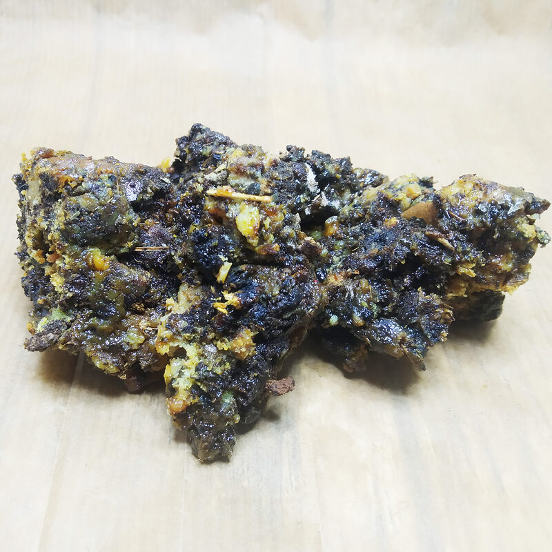 Close-up of dark glossy Fassoukh incense pieces with pale yellow and green fragments on a light wood surface
