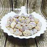 Pale yellow and grey-brown frankincense resin tears piled in a white scalloped ceramic dish on a weathered wood background