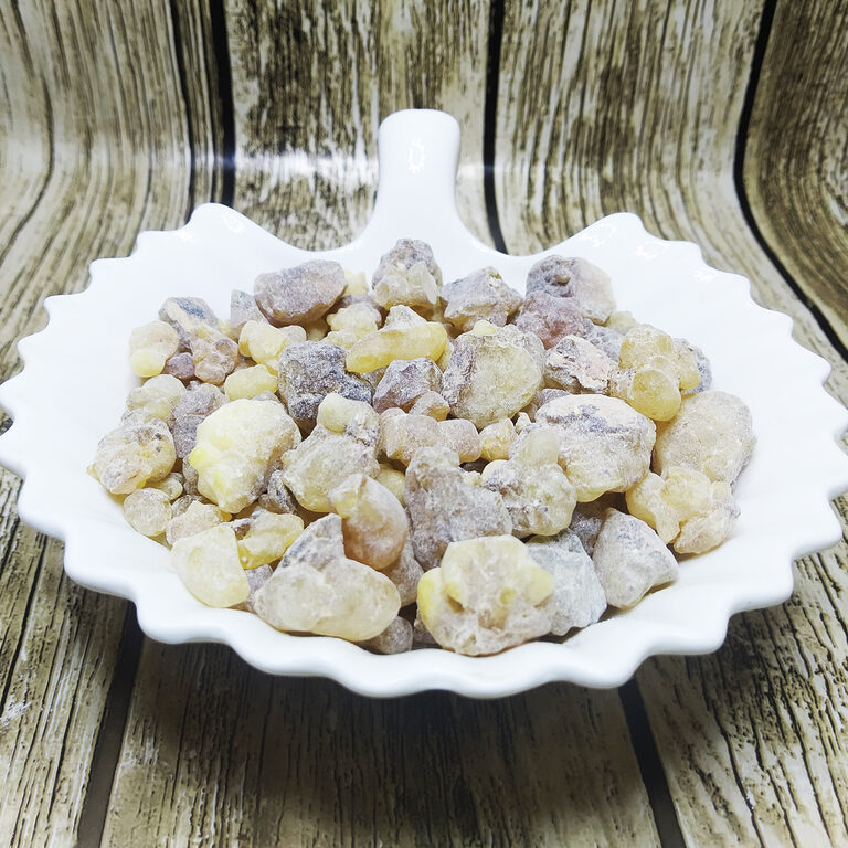 Pale yellow and grey-brown frankincense resin tears piled in a white scalloped ceramic dish on a weathered wood background