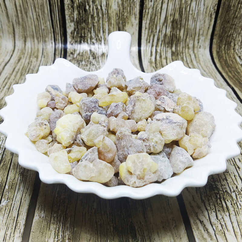 Pale yellow and grey-brown frankincense resin tears piled in a white scalloped ceramic dish on a weathered wood background