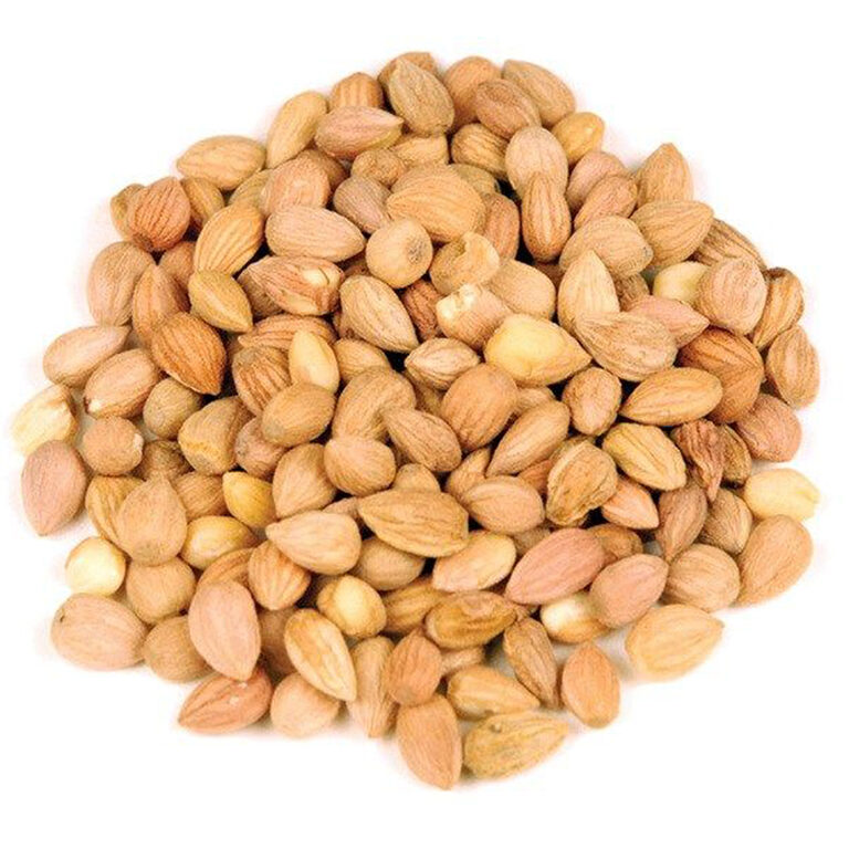 A mound of whole shelled mahaleb kernels with pale tan skins, a few split to show their cream interior, on a white background