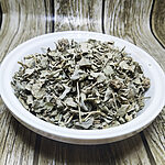 Loose silvery grey-green dried Atriplex halimus leaves with fine stems and small seed clusters in a white bowl on a wood-pattern background