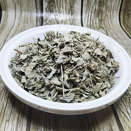 Loose silvery grey-green dried Atriplex halimus leaves with fine stems and small seed clusters in a white bowl on a wood-pattern background