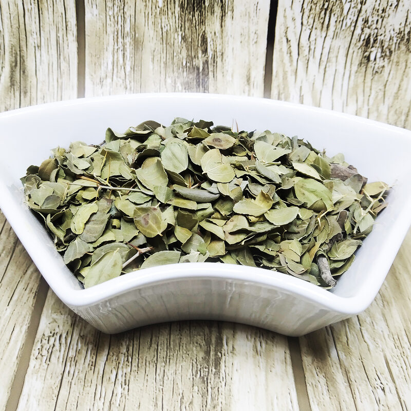Dried green sidr leaves and small twigs in a white dish on a wooden surface