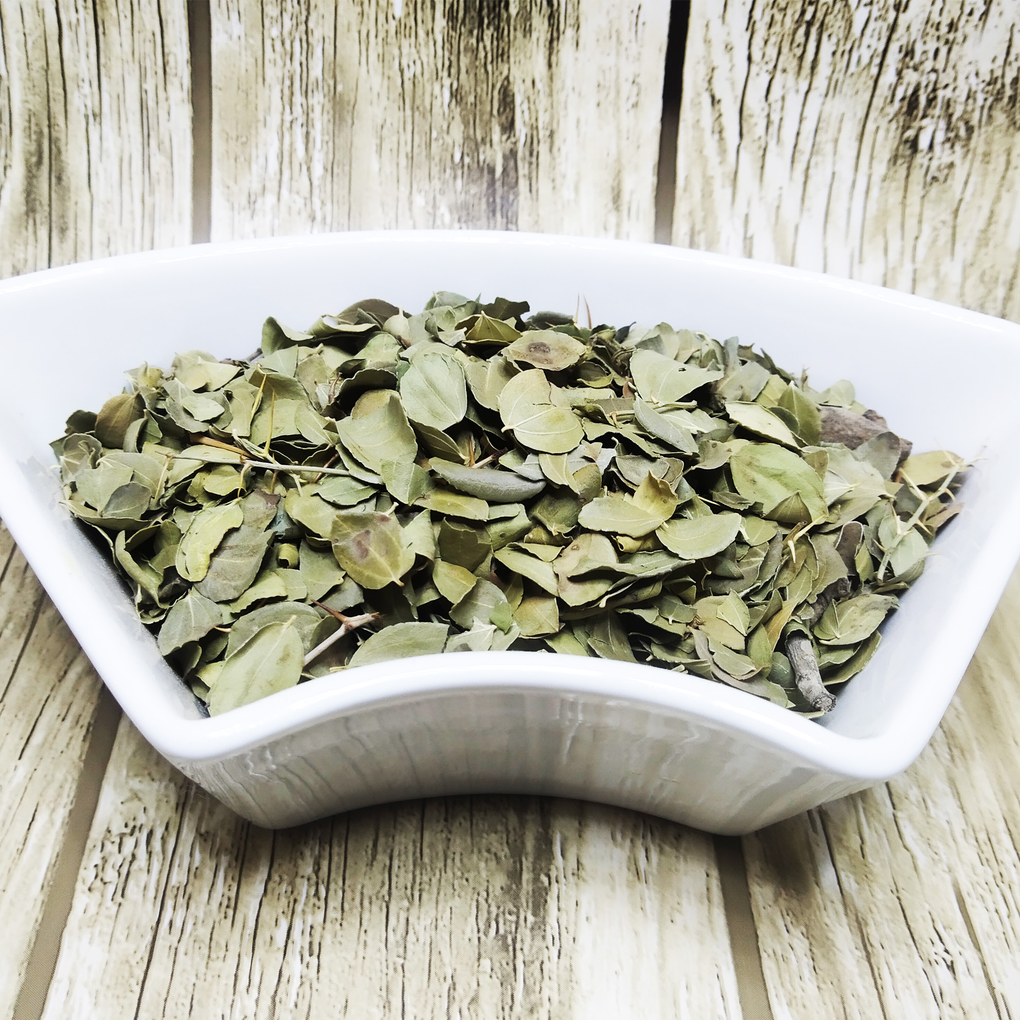 001-Organic-Sidr-Leaves-1 Dried green sidr leaves and small twigs in a white dish on a wooden surface