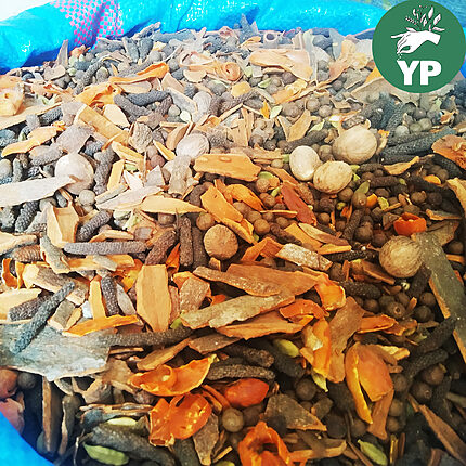 Whole spices heaped in a blue woven sack, with cinnamon bark, long pepper, nutmeg, mace, allspice berries and green cardamom pods