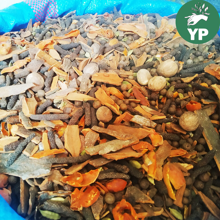 Whole spices heaped in a blue woven sack, with cinnamon bark, long pepper, nutmeg, mace, allspice berries and green cardamom pods