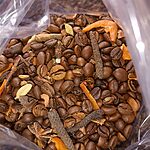 Open clear bag of roasted coffee beans mixed with green cardamom pods, long pepper, star anise, cinnamon bark and dried orange peel