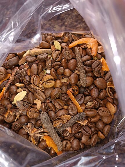 Open clear bag of roasted coffee beans mixed with green cardamom pods, long pepper, star anise, cinnamon bark and dried orange peel