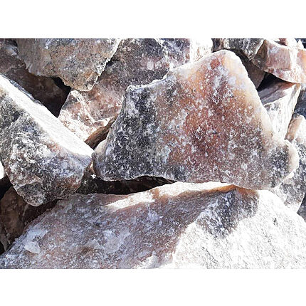 Gros plan sur des morceaux bruts de sel gemme aux tons rose pâle, abricot et gris, avec des plages cristallines blanches, en pleine lumière