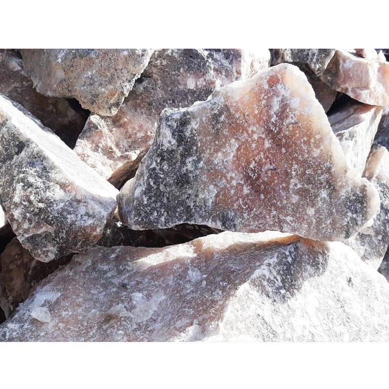 Close-up of raw rock salt chunks in pale pink, apricot and grey tones with white crystalline patches in bright daylight