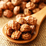 Close-up of wrinkled golden-brown dried tiger nuts heaped on a wooden spoon over burlap, with more tiger nuts blurred in the background