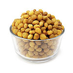 Rounded golden-tan akpi kernels heaped high in a clear glass bowl on a white background