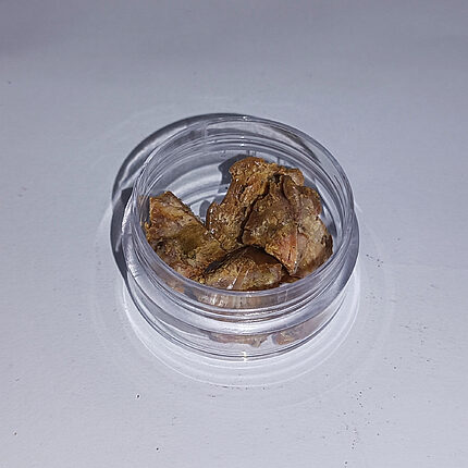 Amber-brown asafoetida resin pieces in a clear jar on a white surface
