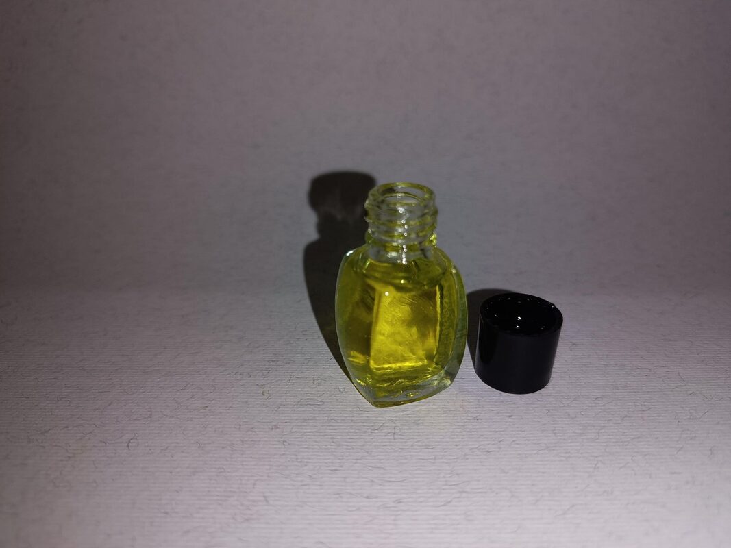 Hand holding a small clear glass bottle of yellow fragrance essence beside its black cap