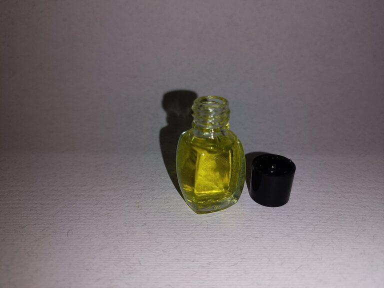 Hand holding a small clear glass bottle of yellow fragrance essence beside its black cap