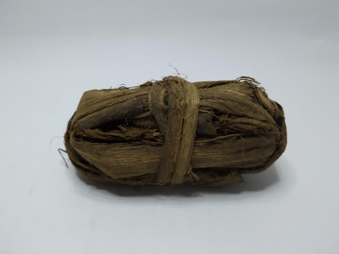 Tied bundle of dark brown fibrous siwak strands on a white background
