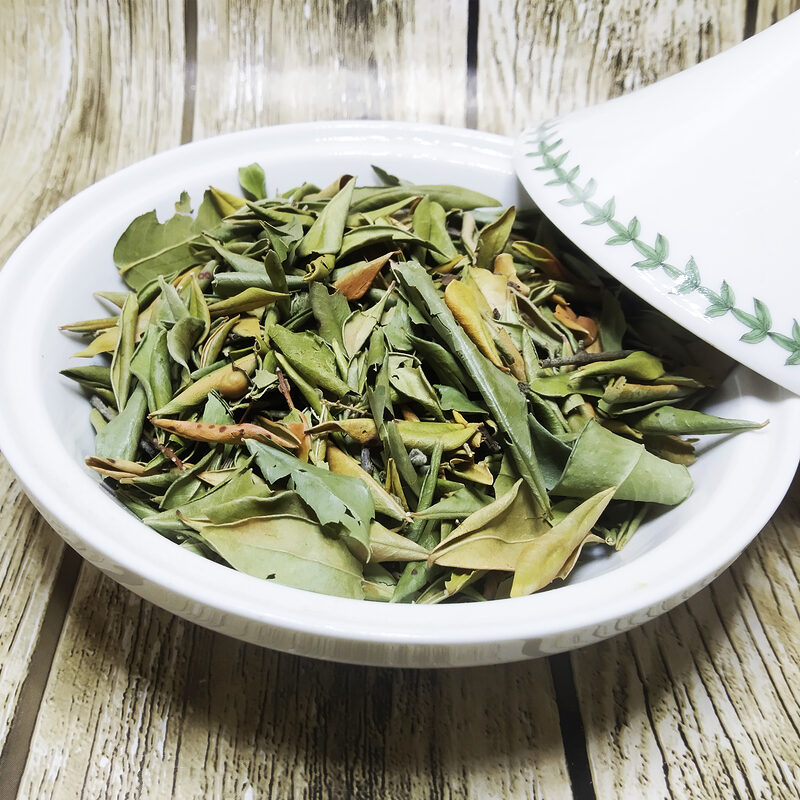 Dried green basil leaves in a white bowl on a wooden surface