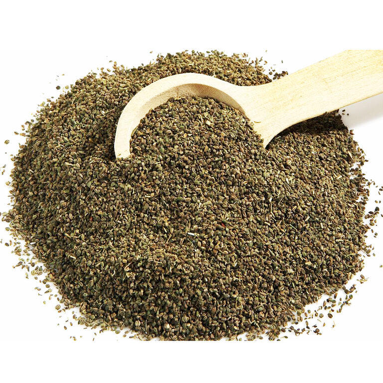 Whole green-brown celery seeds spread beside a wooden scoop on a white background