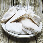 Chalk-white layered cuttlebone pieces piled in a white bowl on a weathered wooden background