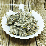 Dried white horehound with woolly silver-grey leaves and white downy stems heaped in a scalloped white ceramic dish on a wood-effect background