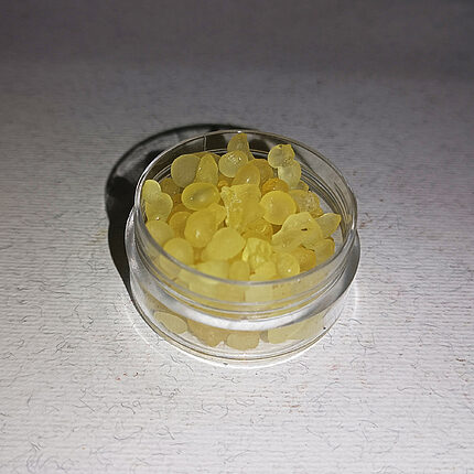 Pale yellow mastic resin tears, frosted and partly translucent, filling a small clear round jar on a white textured surface.