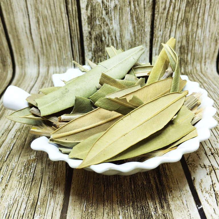 Long sage-green dried oleander leaves and a few stem pieces heaped in a white scalloped dish with a small white scoop, against weathered wood
