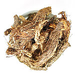 Pile of dried brown spikenard root pieces covered in reddish hair-like fibres, in a white bowl seen from above