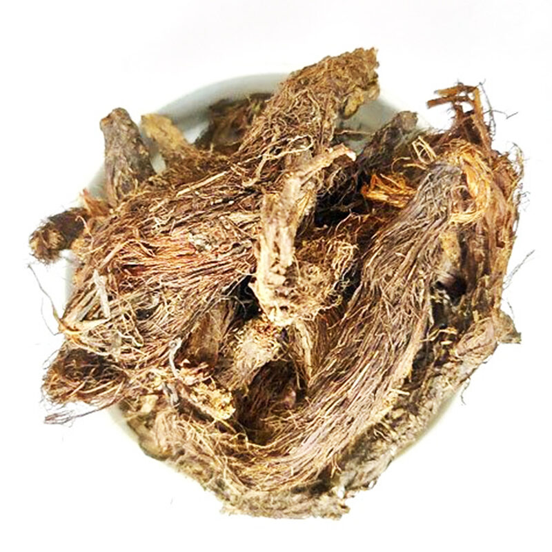 Pile of dried brown spikenard root pieces covered in reddish hair-like fibres, in a white bowl seen from above