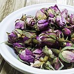 Boutons de rose séchés rose-violet entiers avec sépales verts dans un bol blanc sur une surface en bois