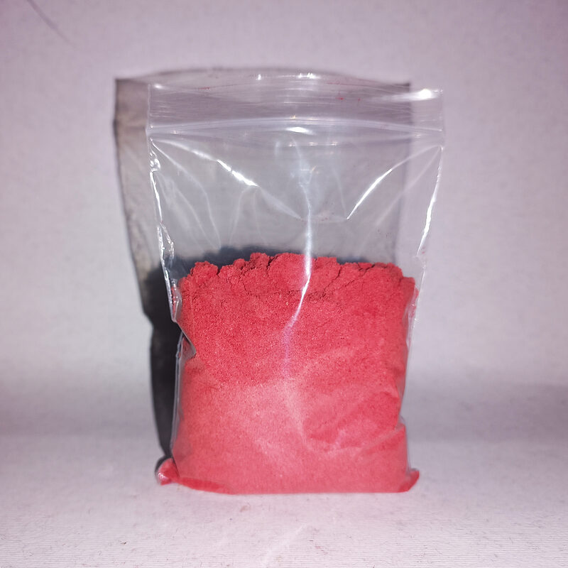 A resealable clear bag holding finely milled bright rose-red Soqla powder, stood on a pale surface.
