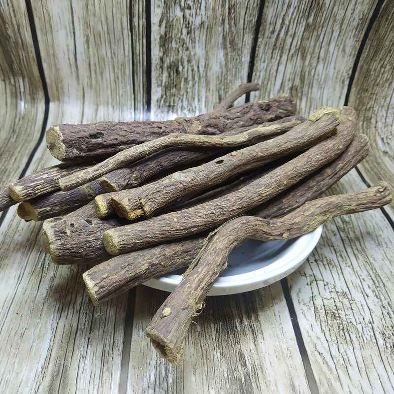 Long dried licorice root sticks piled on a white plate over a wood-grain surface.