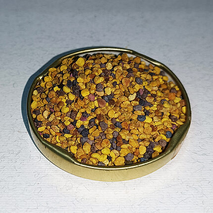 Mixed yellow, orange, brown and purple bee pollen granules in a shallow brass dish.