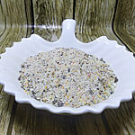 Coarse pale incense powder with yellow, amber and darker flecks in a white scalloped dish.