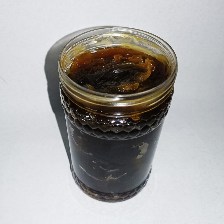 Open clear jar filled with glossy dark brown black soap paste on a white surface