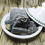 Irregular charcoal-black mineral chunks with exposed yellow areas on a white plate beside a white floral-patterned dish
