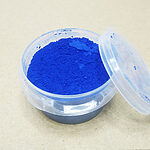 Clear plastic tub filled with vivid blue fine powder, with its lid leaning beside it on a light surface.