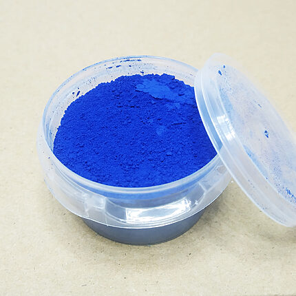 Boîte transparente remplie d’une fine poudre bleu vif, avec son couvercle posé à côté sur une surface claire.