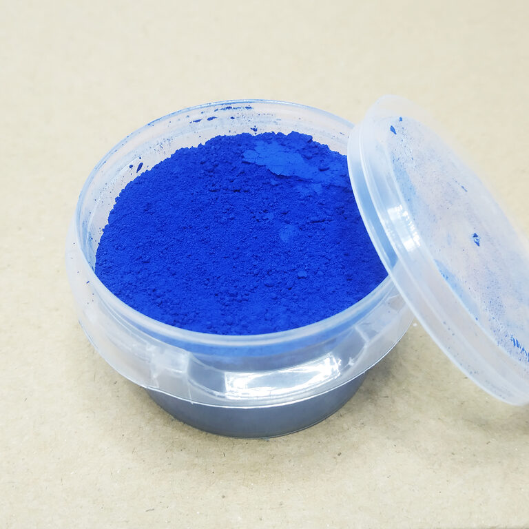 Clear plastic tub filled with vivid blue fine powder, with its lid leaning beside it on a light surface.