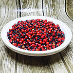 Bowl filled with glossy red-and-black Abrus precatorius seeds on a wood-grain surface