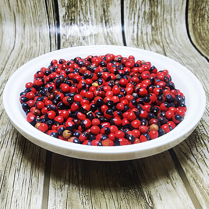 Bowl filled with glossy red-and-black Abrus precatorius seeds on a wood-grain surface