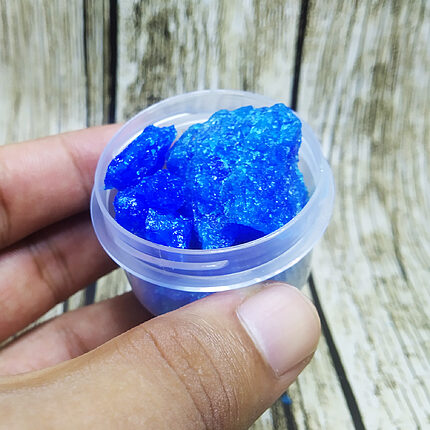 Cristaux grossiers bleu vif de sulfate de cuivre dans une petite coupelle transparente tenue à la main.