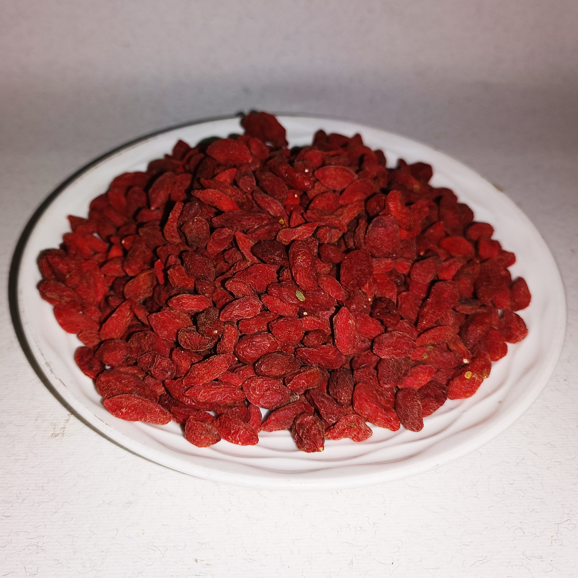 001-v-34 Baies de goji séchées rouge foncé disposées sur une assiette blanche