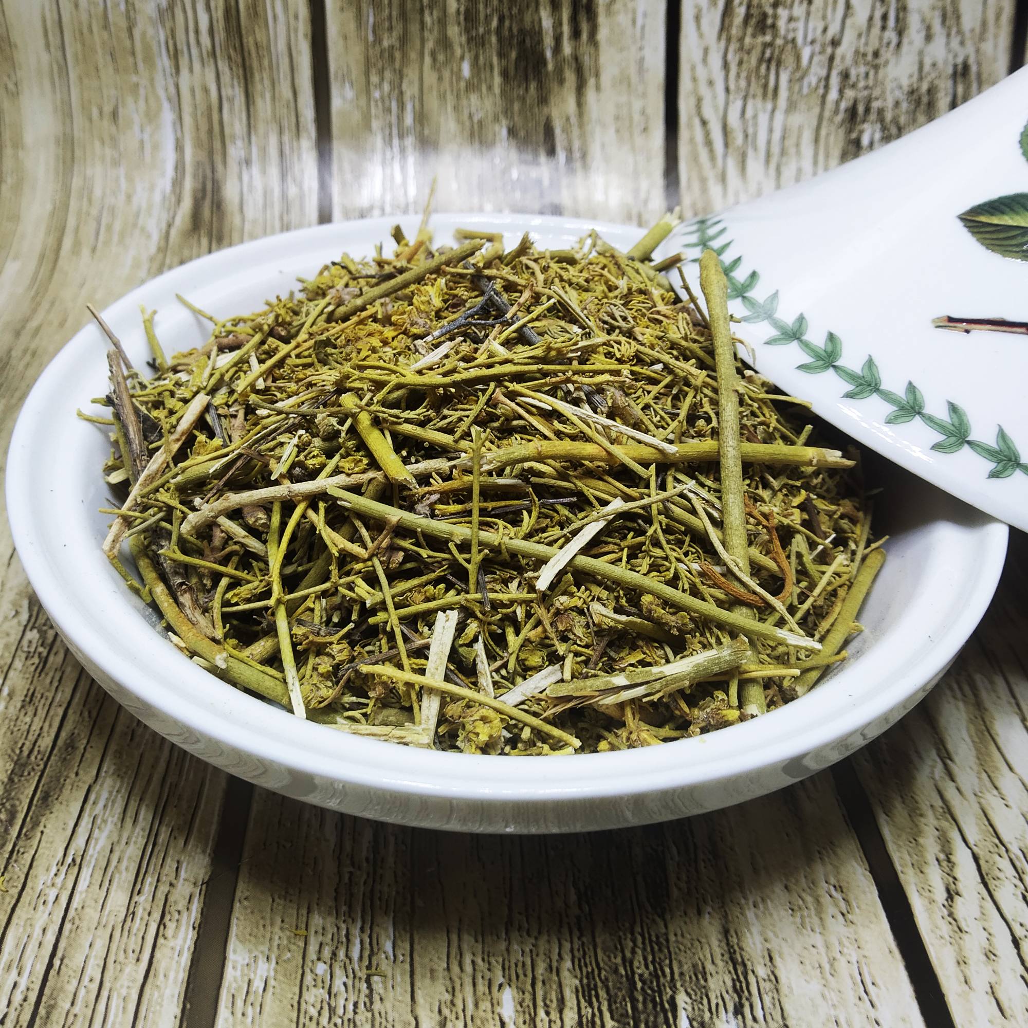 001-v-38 Bowl filled with green dried rue stems, leaves and flower tips beside a white spoon
