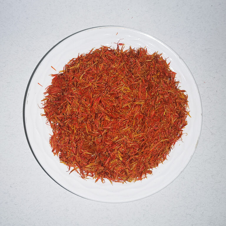 Loose orange-red dried safflower petals piled on a round white plate