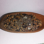 Coarse dark incense blend with seeds, dried fragments and translucent pieces in a wooden spoon